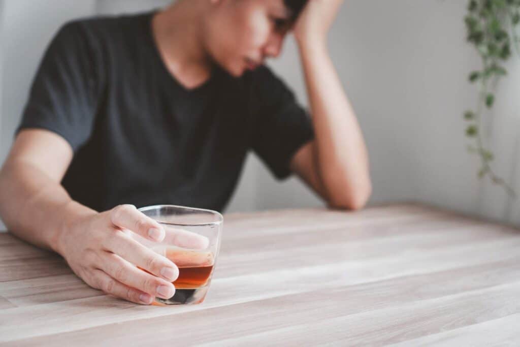 Person holding a glass of alcohol while appearing emotionally distressed, illustrating the early warning signs of alcohol addiction.