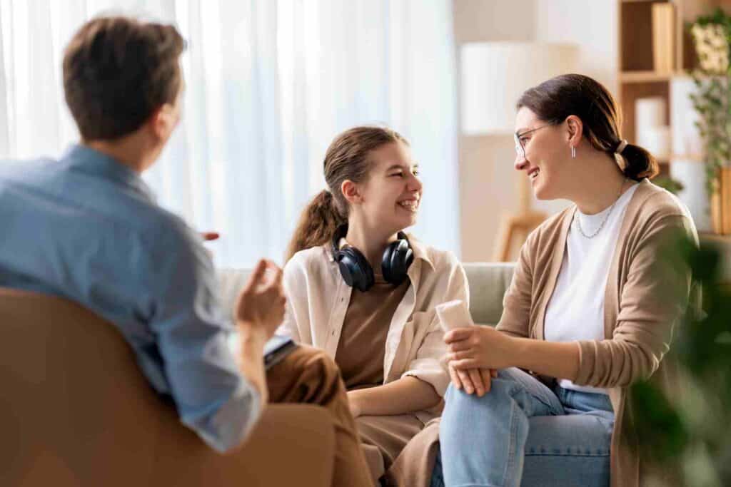 Family Therapy: Healing Relationships During Recovery 1 Parents and their teenage daughter smiling together during a family therapy session for addiction recovery.