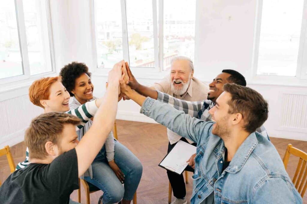 Group therapy session in rehab with diverse patients doing a high five showing support and recovery progress