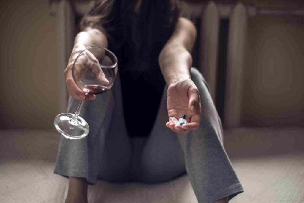 Person holding a glass of wine and prescription pills, illustrating the dangers of mixing alcohol with medications and substance misuse.