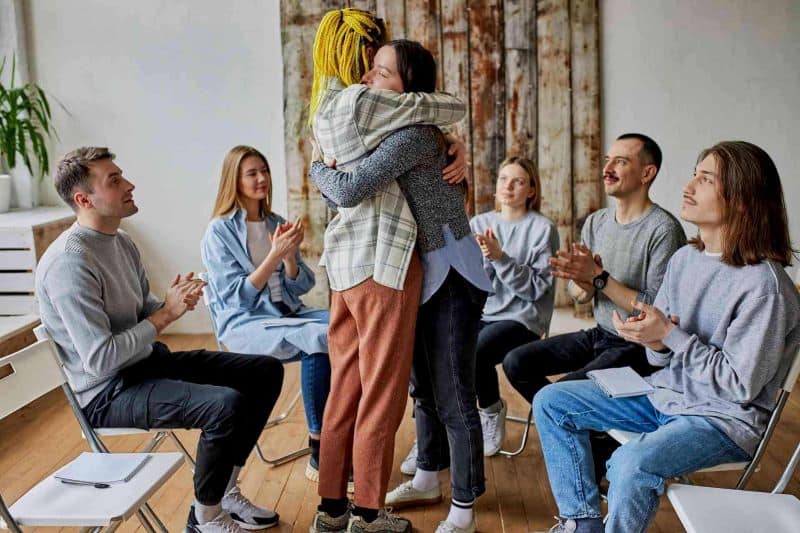 People in a rehab group support session hugging and celebrating recovery progress